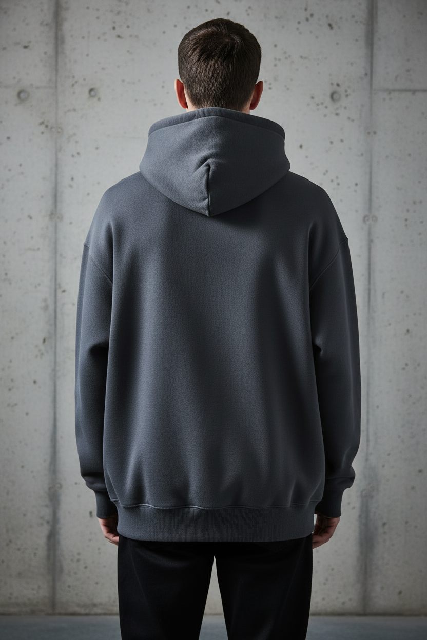 Oversized heavyweight charcoal hoodie back view on model against concrete wall